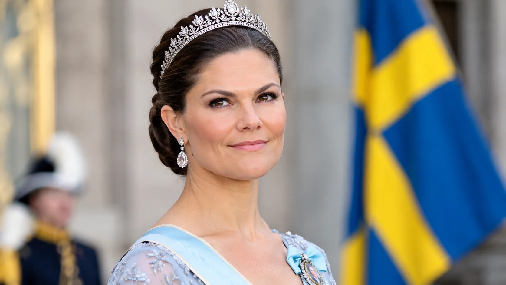 Victoria von Schweden in einem eleganten hellblauen Kleid mit Tiara vor einer schwedischen Flagge