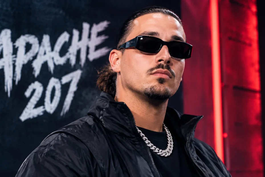 Apache 207 wearing sunglasses and performing in a dark urban setting